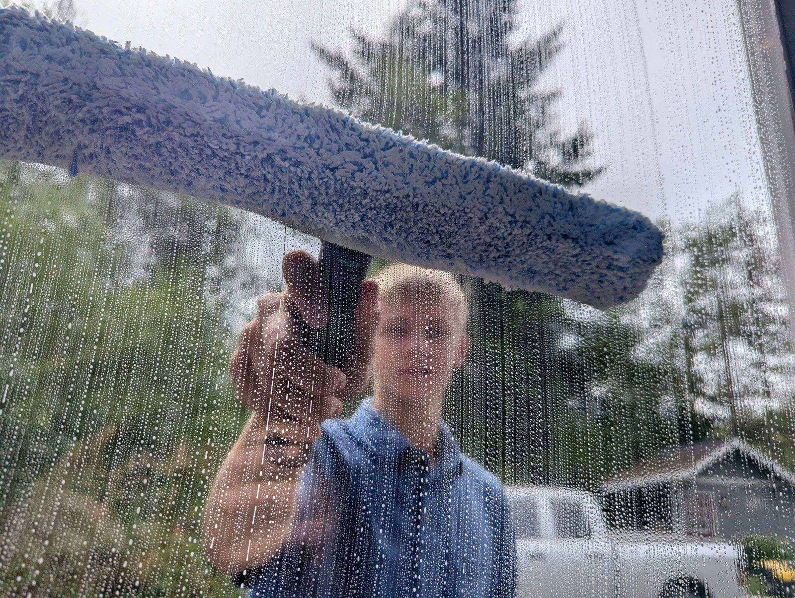 Close-up shot through a soapy, water-streaked window with a squeegee tool mid-clean