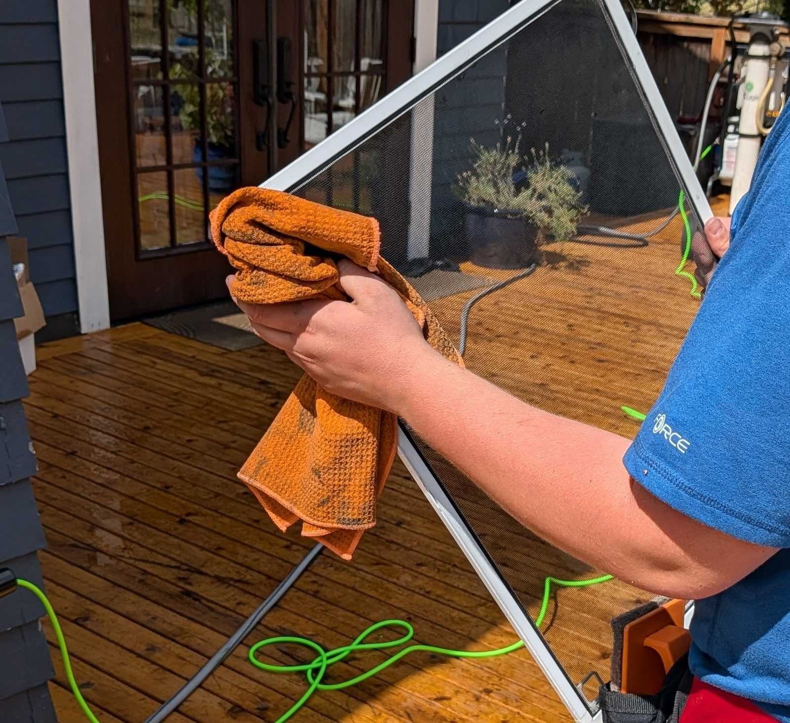 Technician wiping down a window screen with a microfiber cloth on an outdoor deck