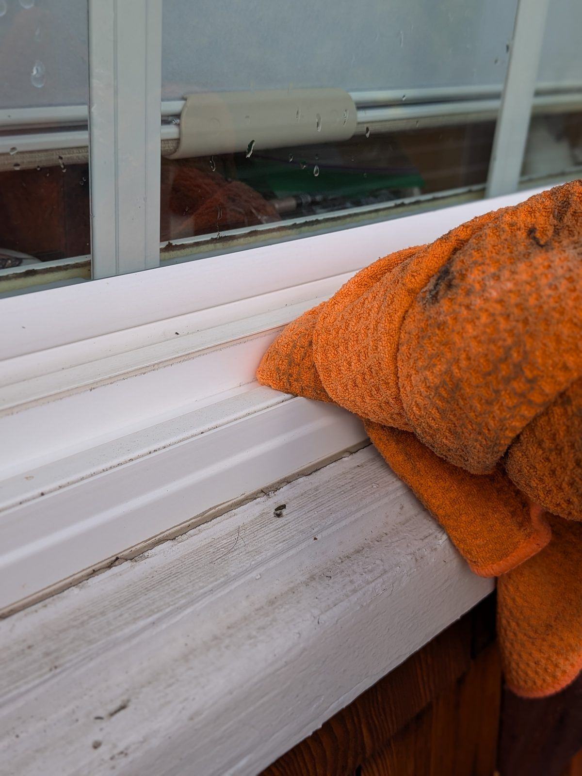Close-up of a window track and sill being wiped clean with a microfiber cloth